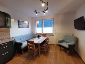 Un espace de vie compact comprenant un coin cuisine, un coin repas avec une table et des chaises, un canapé et un téléviseur fixé au mur.