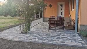 Une terrasse avec une table et des chaises, un banc et une porte donnant accès à un bâtiment.