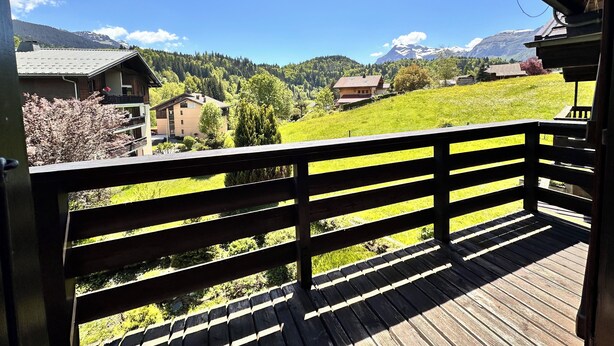 Un balcón de madera con vistas a una ladera verde y casas.