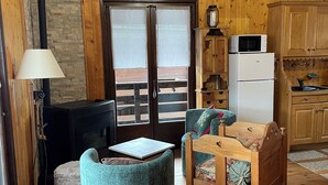Una habitación acogedora con paredes y suelos de madera, un sofá, una mesa, una lámpara y una zona de cocina con refrigerador y microondas.