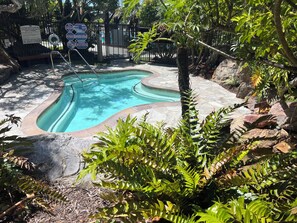 A swimming pool with a stone border, surrounded by tropical plants and a fence. - Oceanview Retreat at North Coast Village B107 (Oceanside)