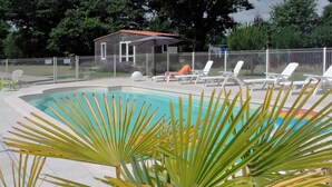 Piscina com espreguiçadeiras e um pequeno edifício ao fundo.