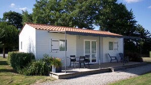 Uma casa pequena, térrea, com telhado de cerâmica, varanda coberta com área de estar externa e entrada por caminho de pedras.