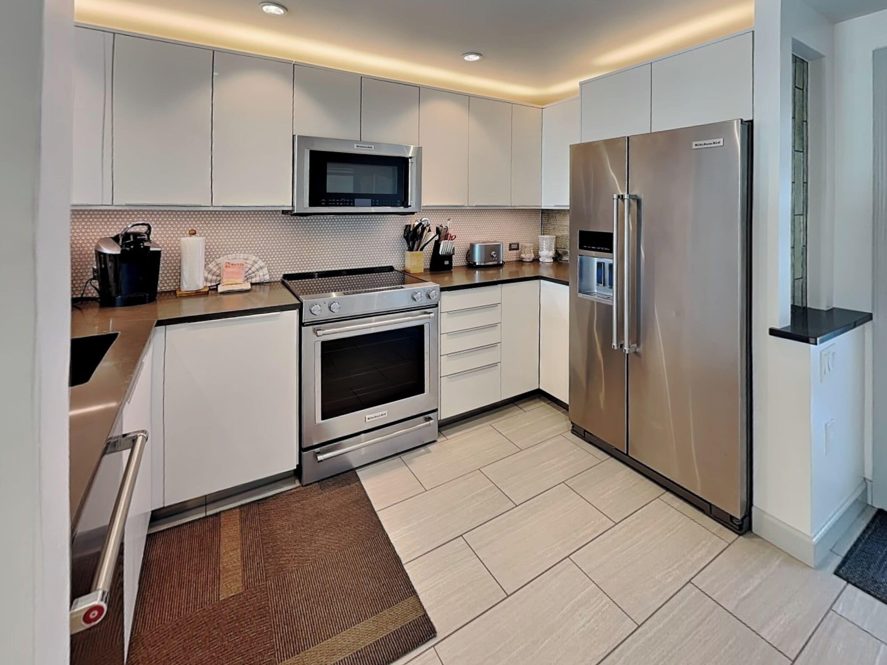 A modern kitchen with stainless steel appliances, white cabinetry, and a tiled backsplash.