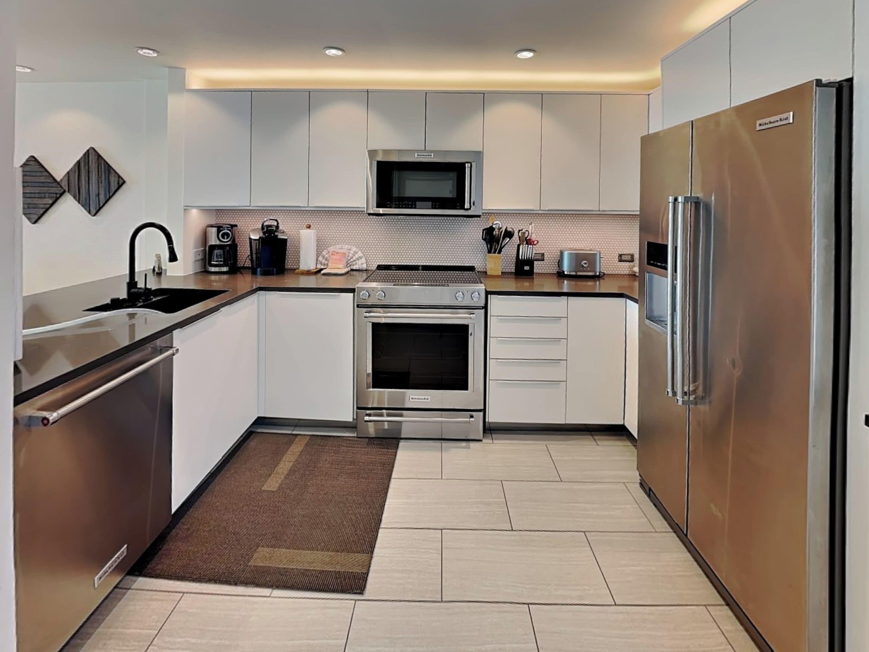 A modern kitchen with stainless steel appliances, white cabinetry, and a tiled backsplash.