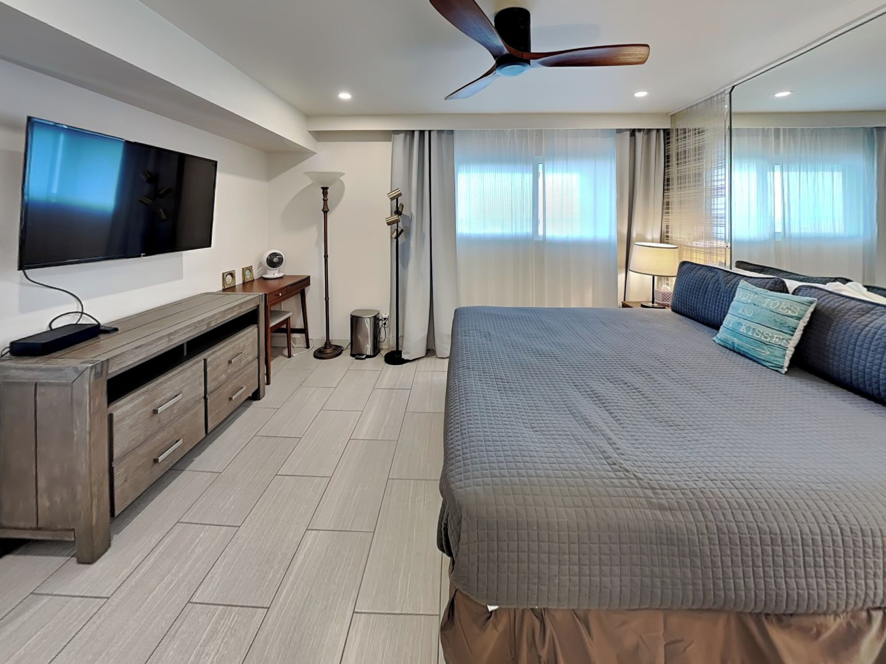 A modern hotel room with a large bed, a flat-screen TV, a desk, and a ceiling fan.