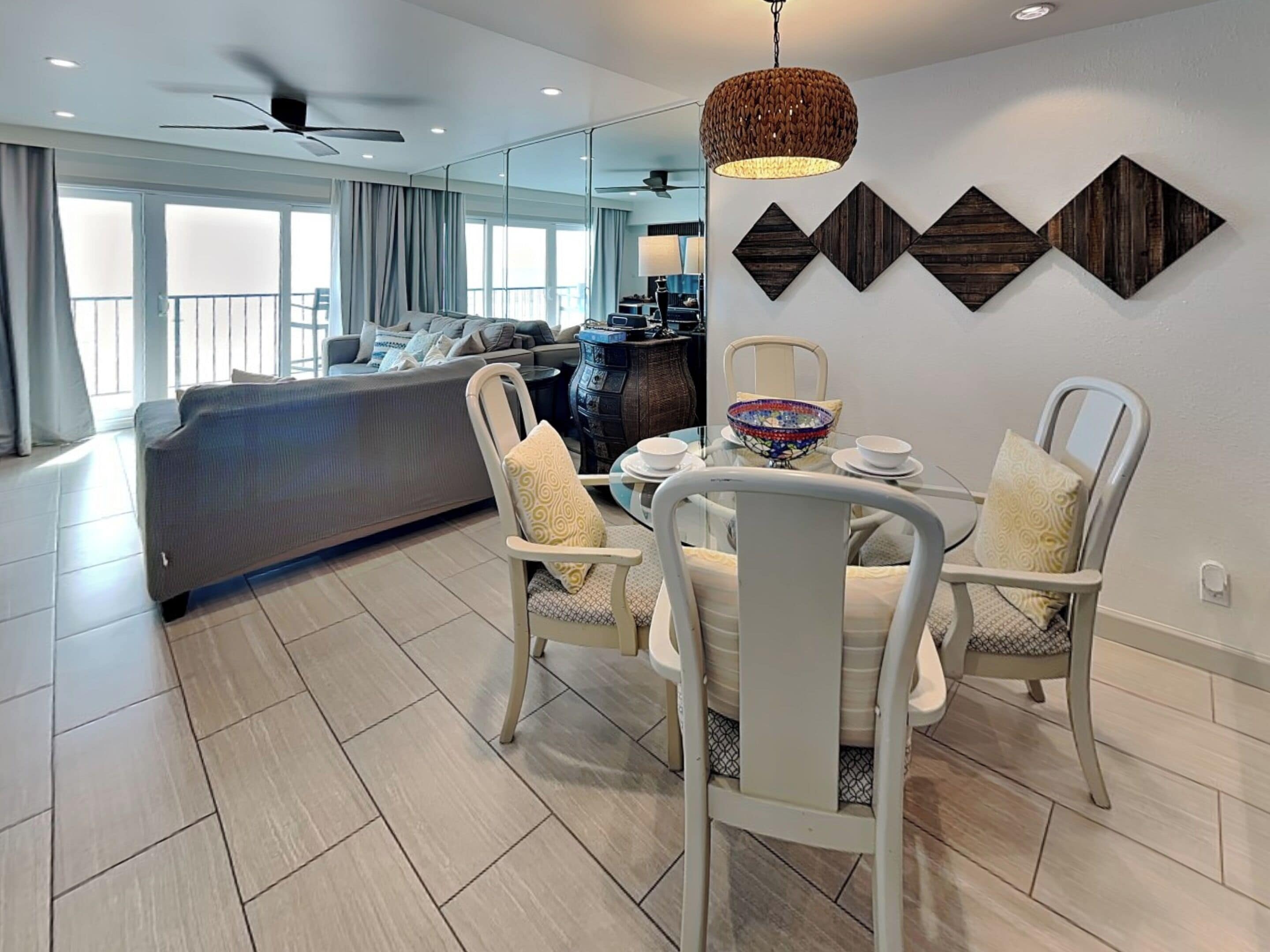 A modern living room with a sofa, dining table, and chairs. There is a ceiling fan and a decorative wall piece above the table.
