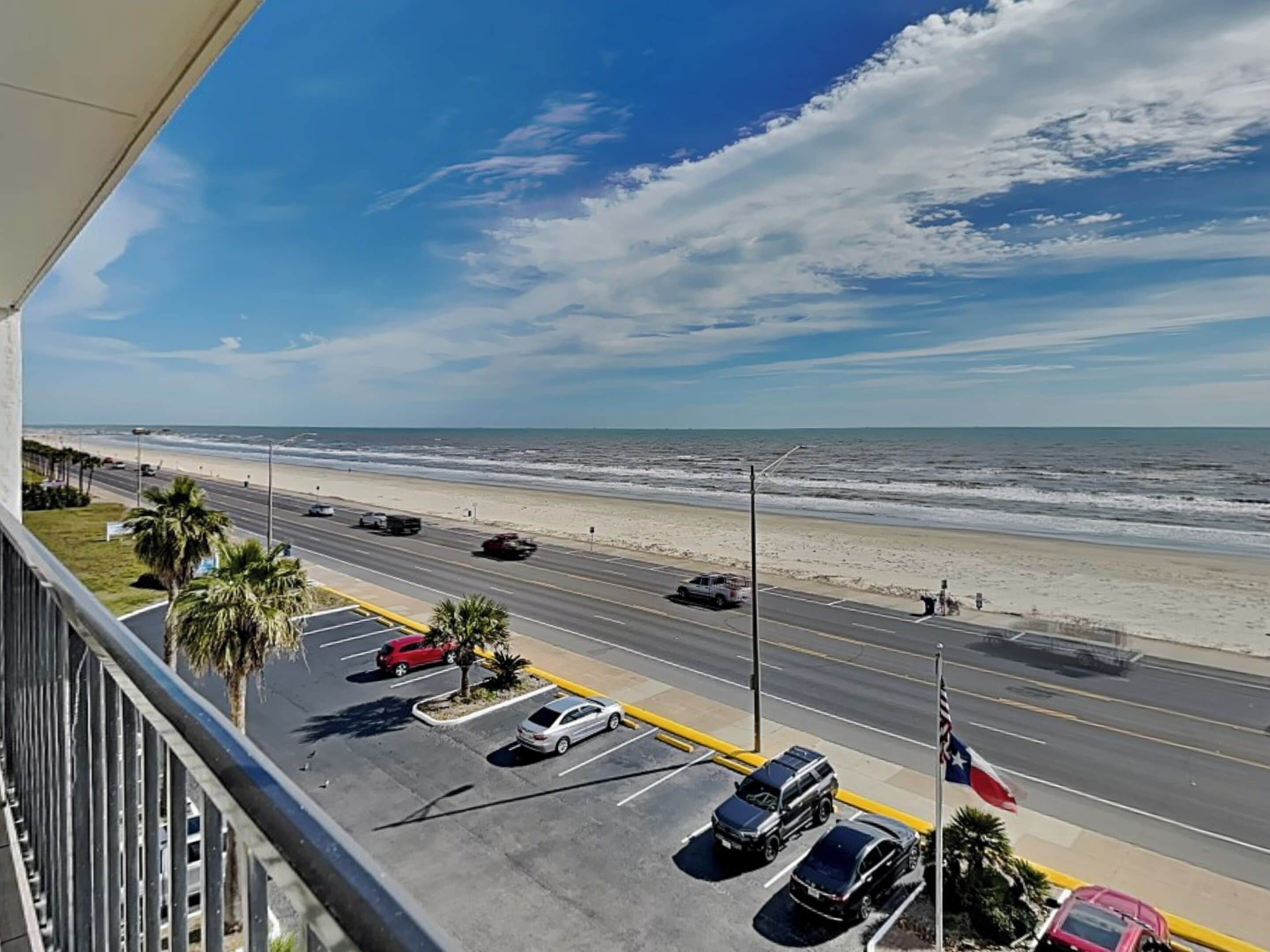 A view from a balcony overlooking a beach with a road and parked cars.