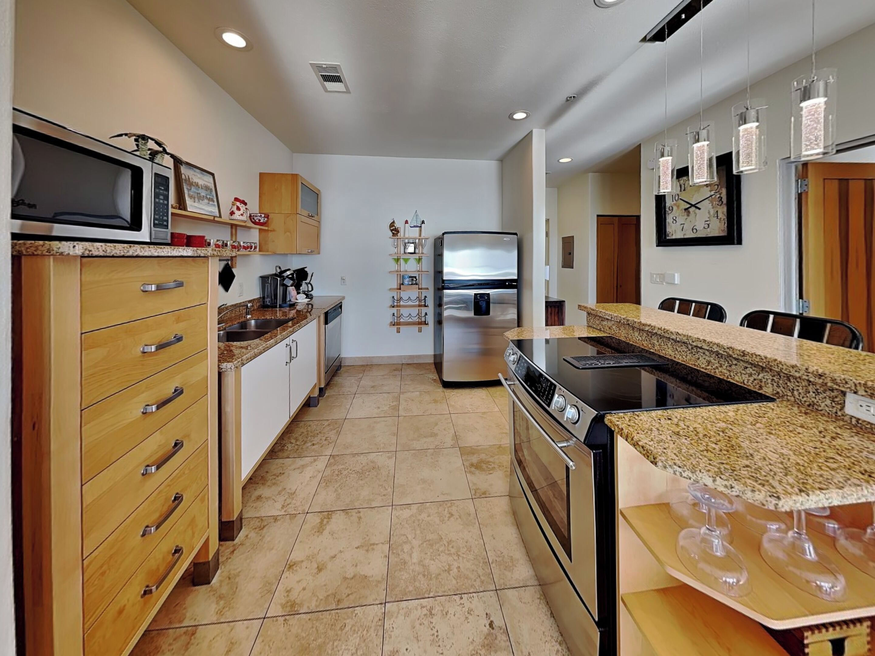 A modern kitchen with wooden cabinets, a stainless steel refrigerator, a built-in oven, and a granite countertop.