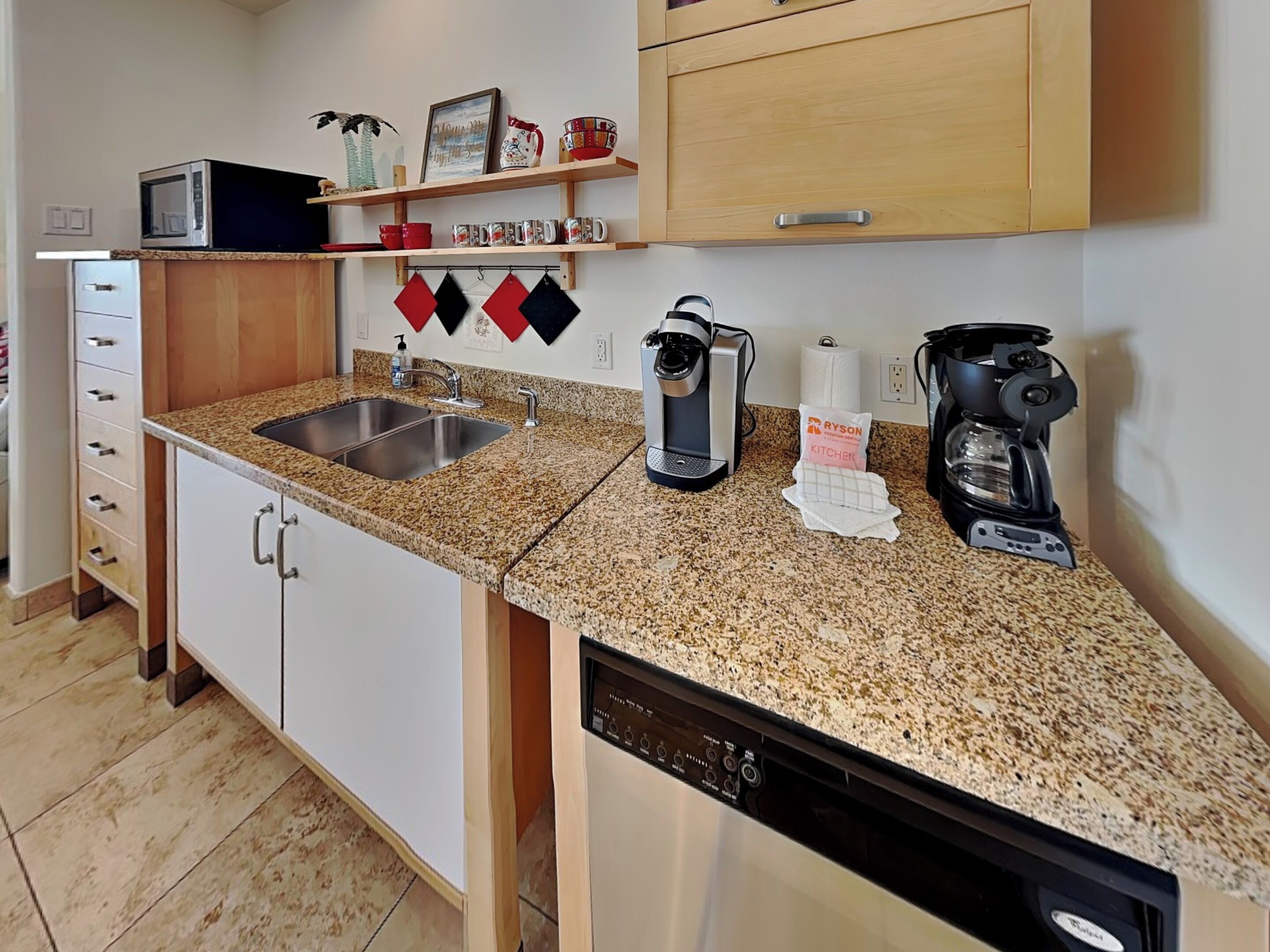Una cocina con encimeras de granito, lavavajillas, cafetera y microondas.