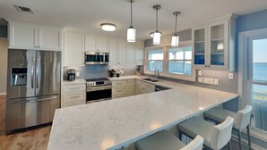 Una cocina moderna con armarios blancos, electrodomésticos de acero inoxidable, una isla de mármol y taburetes de bar.