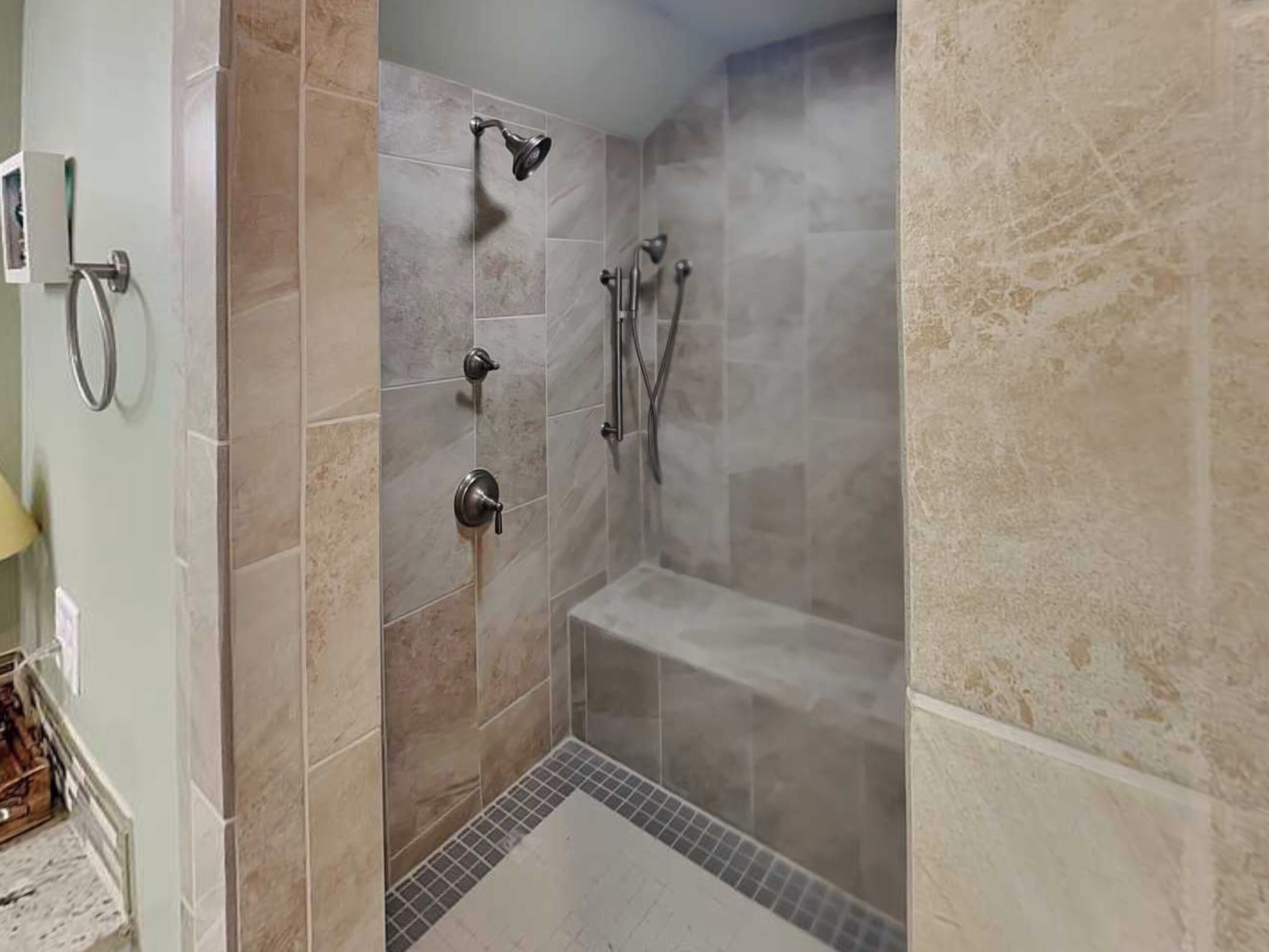 A shower with a handheld showerhead, a wall-mounted faucet, and a handheld showerhead.