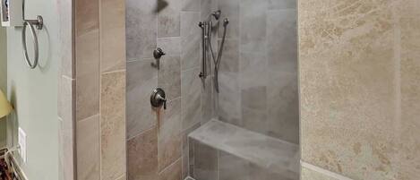 A shower with a handheld showerhead, a wall-mounted faucet, and a handheld showerhead.