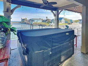 Un espace extérieur abrité comprenant une table de billard, un ventilateur de plafond et une vue sur une marina avec des bateaux et des maisons.