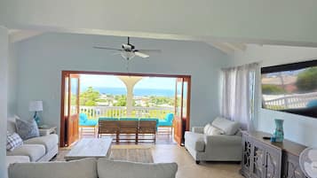 Un salon avec un canapé, une table basse et un téléviseur. Il y a un balcon avec vue sur l’océan.