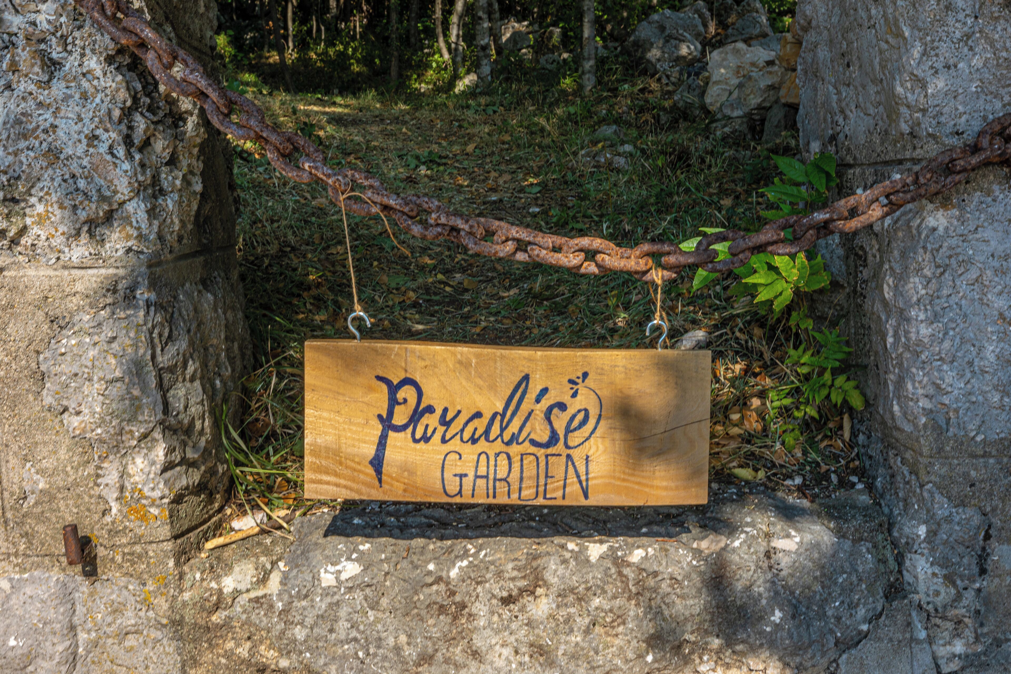 Un letrero de madera con el texto 'Paradise Garden' colgado de una enredadera.