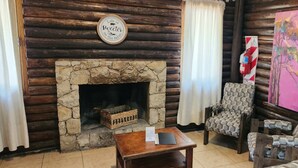 Interior acolhedor de uma cabana de madeira com lareira de pedra, cadeiras estampadas e uma mesa de madeira.