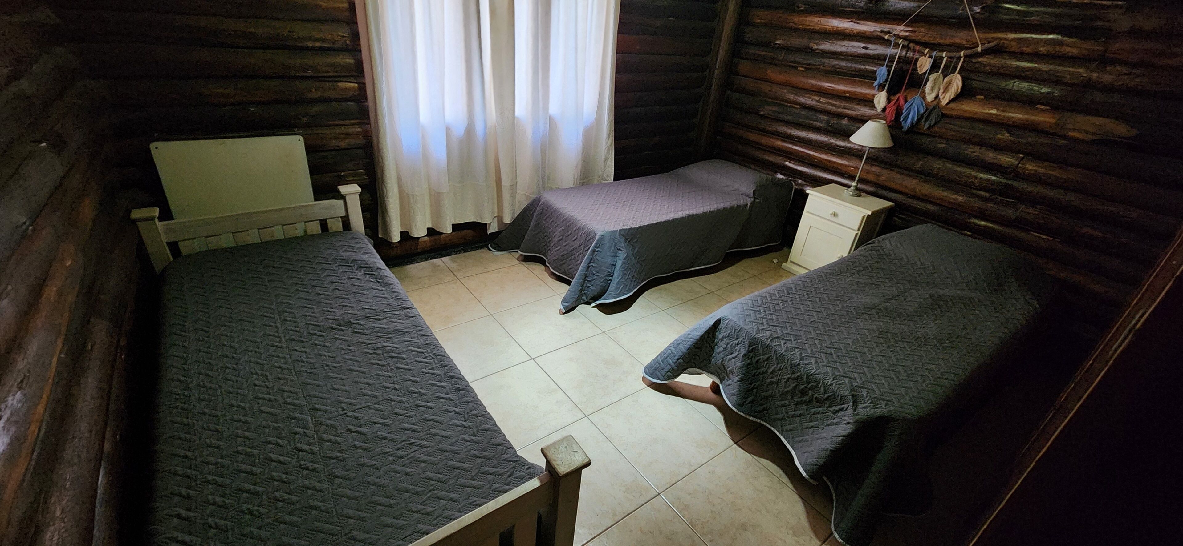 Une chambre de style cabane avec deux lits simples, une petite table, une chaise et une lampe.
