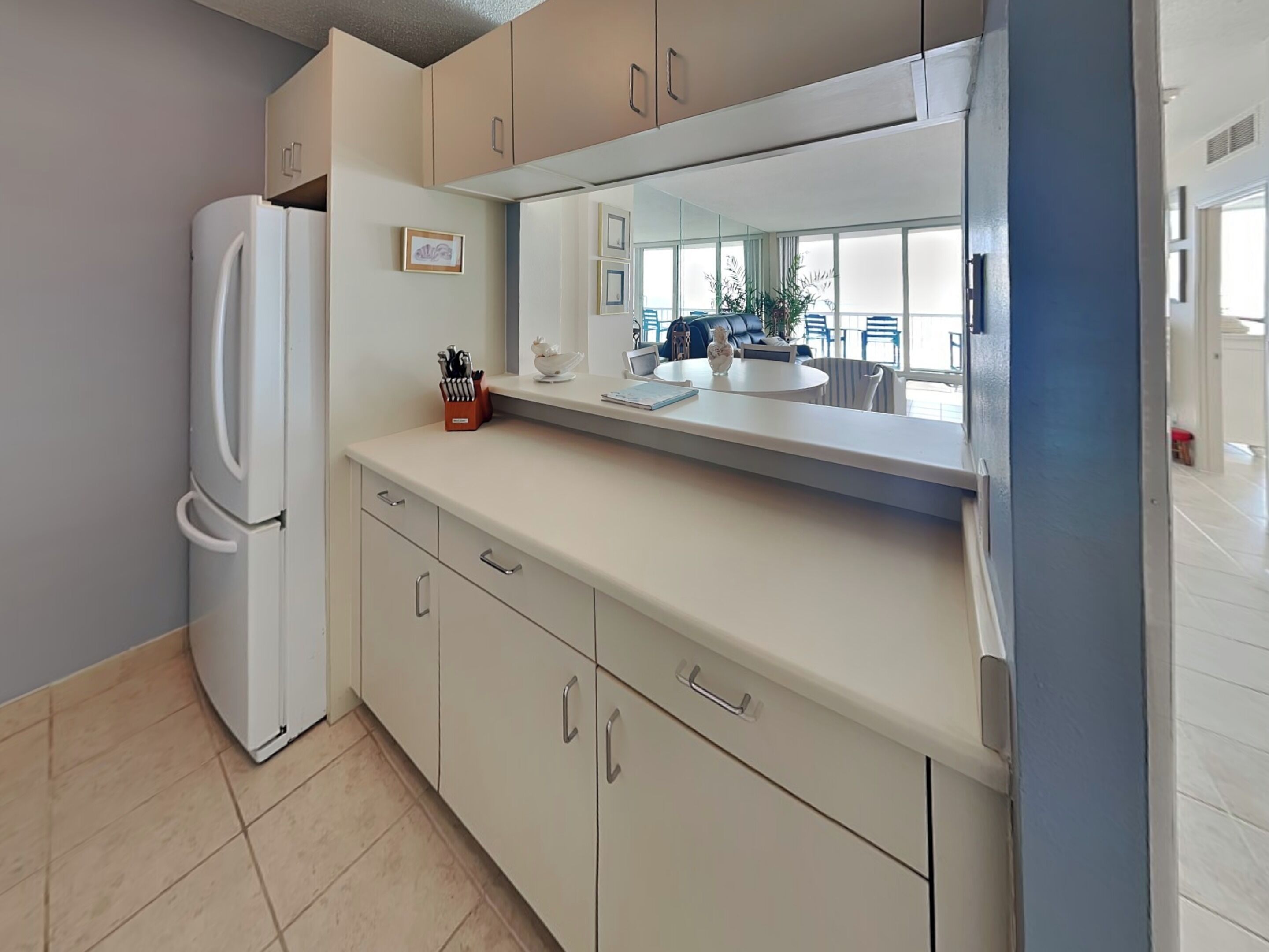 Una cocina moderna con un refrigerador blanco, gabinetes color beige y un espejo grande sobre la encimera.