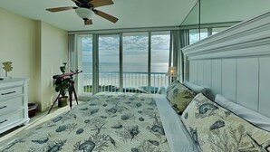 A bedroom with a large bed, a ceiling fan, a dresser, and a view of the ocean through large windows. - Galvestonian 1103 - Endless Sea (Galveston)