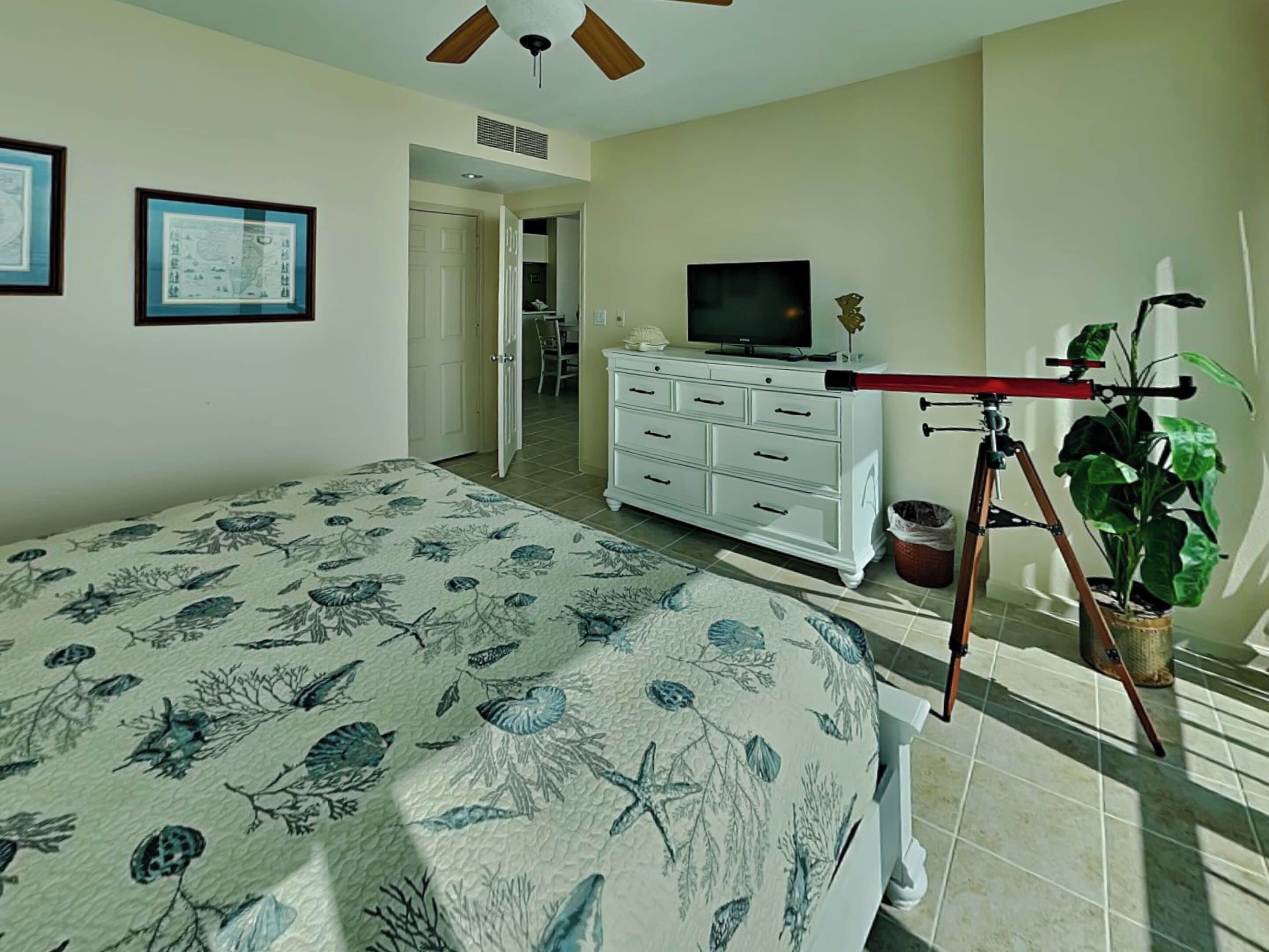 A bedroom with a bed, dresser, TV, and a tripod with a camera.