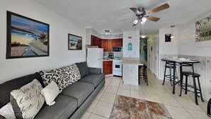 A modern living room with a grey sofa, a patterned throw pillow, and a large painting of a beach scene. - Casa Del Mar 394-stress Free Zone (Galveston)