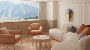 A modern living room with a view of mountains, a sofa, armchairs, and a small round table. - Hotel Londres (Caracas)