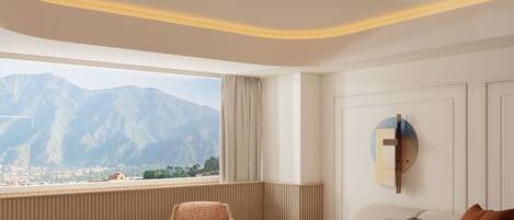 A modern living room with a view of mountains, a sofa, armchairs, and a small round table.