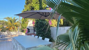 An outdoor patio with a table and chairs, surrounded by lush greenery and a stone structure. - Villa Palma with magnificent unobstructed view of the mountain (VC)