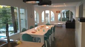 A modern dining area with a long table, chairs, and a kitchen area with a sink. - Villa Palma with magnificent unobstructed view of the mountain (VC)