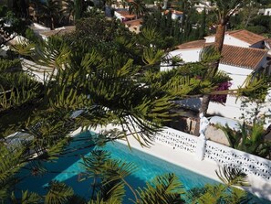 Ein Pool, umgeben von üppiger Vegetation und weißen Gebäuden mit Terrakotta-Dächern.