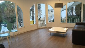 A spacious room with large arched windows, a wooden floor, a central table, and a sofa. - Villa Palma with magnificent unobstructed view of the mountain (VC)