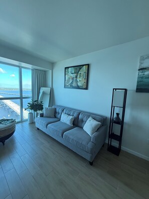 A living room with a grey sofa, a floor lamp, and a painting on the wall. - Luxury II | Breathtaking 24th-floor view of the Caloosahatchee River (fort myers)