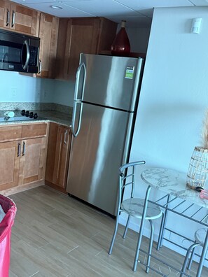 A kitchen with wooden cabinets, a stainless steel refrigerator, a microwave, and a marble countertop. - Luxury II | Breathtaking 24th-floor view of the Caloosahatchee River (fort myers)