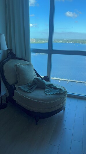 Quarto com uma grande janela que oferece vista para o mar e edifícios distantes.