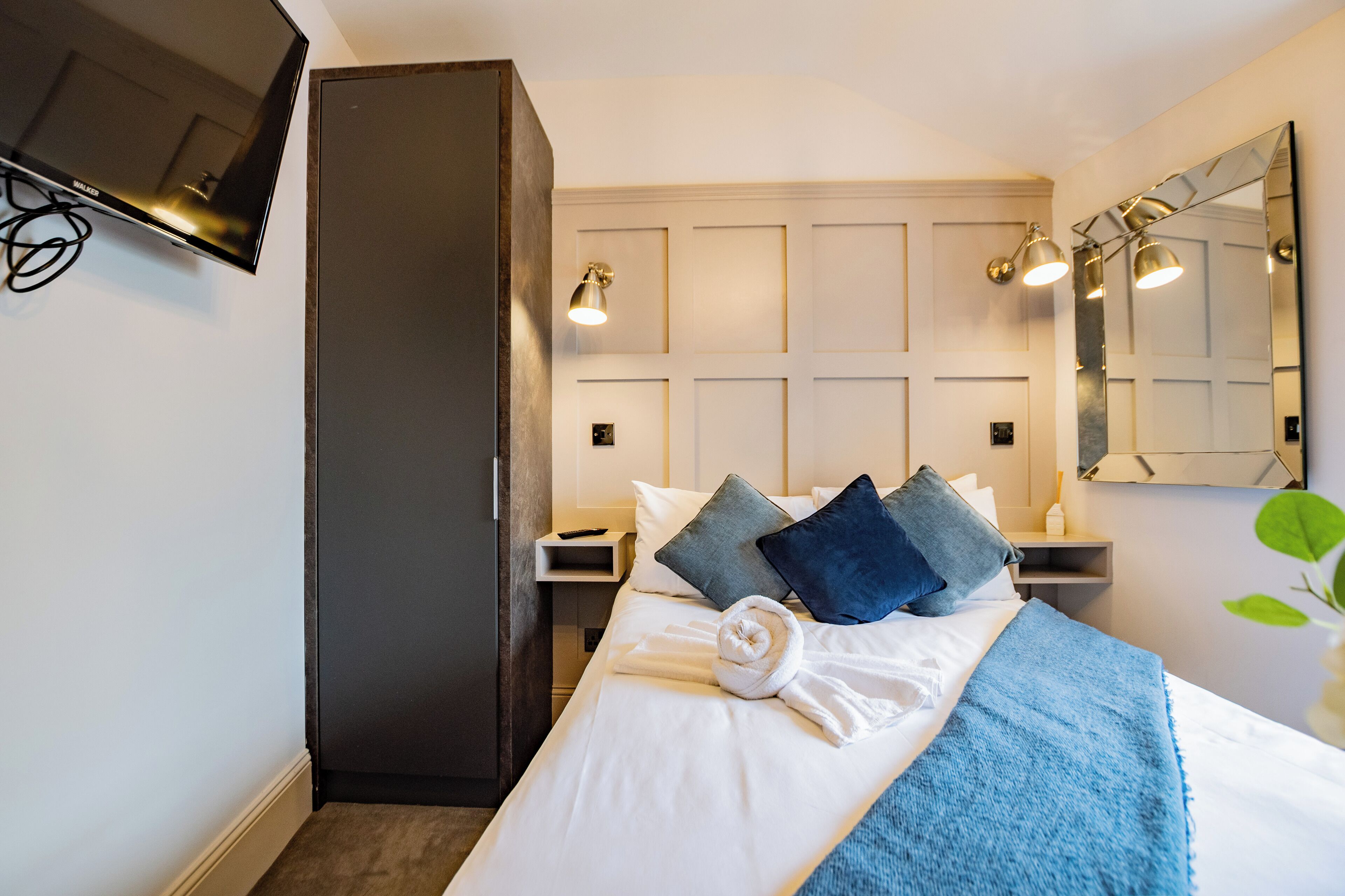 A hotel room with a bed, a wardrobe, a TV, bedside lamps, and a mirror.