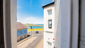 A view from a window overlooking a street with a blue building, a road, and a beach in the distance. - Superb Studio with Marina Views (Howth)