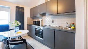 A modern kitchen with a built-in oven, microwave, and sink. There is a dining table with chairs and a vase of flowers. - Superb Studio with Marina Views (Howth)