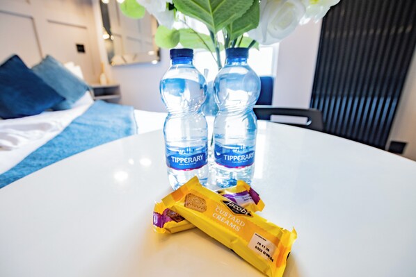 Un tavolo con due bottiglie d'acqua, una confezione di Jacobs Custard Creams e un vaso con fiori.