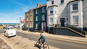 A street with a person riding a bicycle, parked cars, and buildings with a staircase leading to a door. - Superb Studio with Marina Views (Howth)