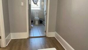 Corridoio che conduce a un bagno con il water, un cestino e una zona doccia.