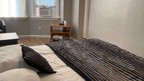 Una camera da letto con un letto, un comodino di legno e una finestra con condizionatore.