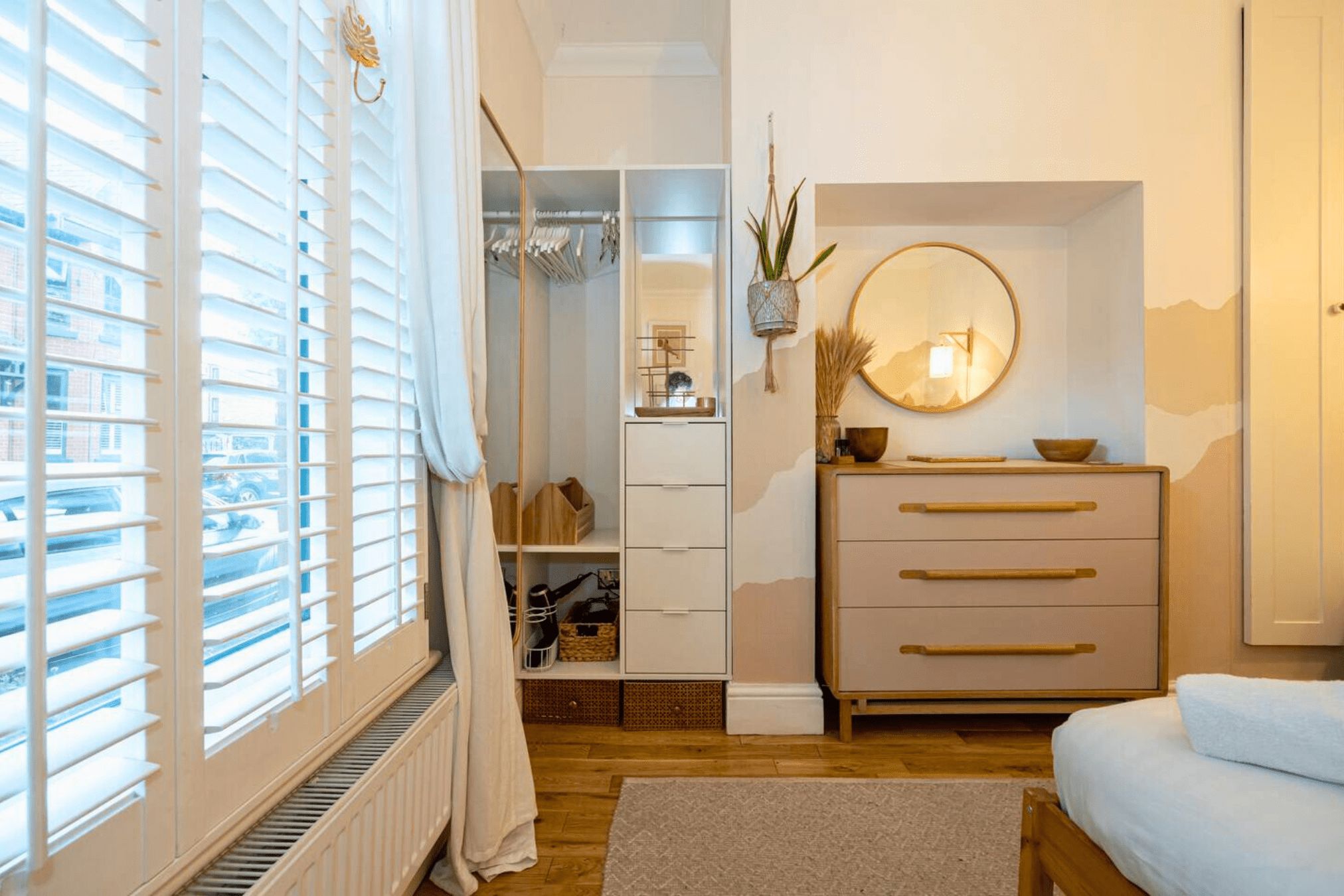 Ein Schlafzimmer mit Bett, Kommode, Spiegel und Kleiderschrank mit Kleidung.