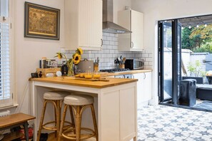A kitchen with a bar area, white cabinets, a tiled backsplash, and a view through a glass door. - 1BDR House | Free Parking | Private Outdoor Space (Manchester)