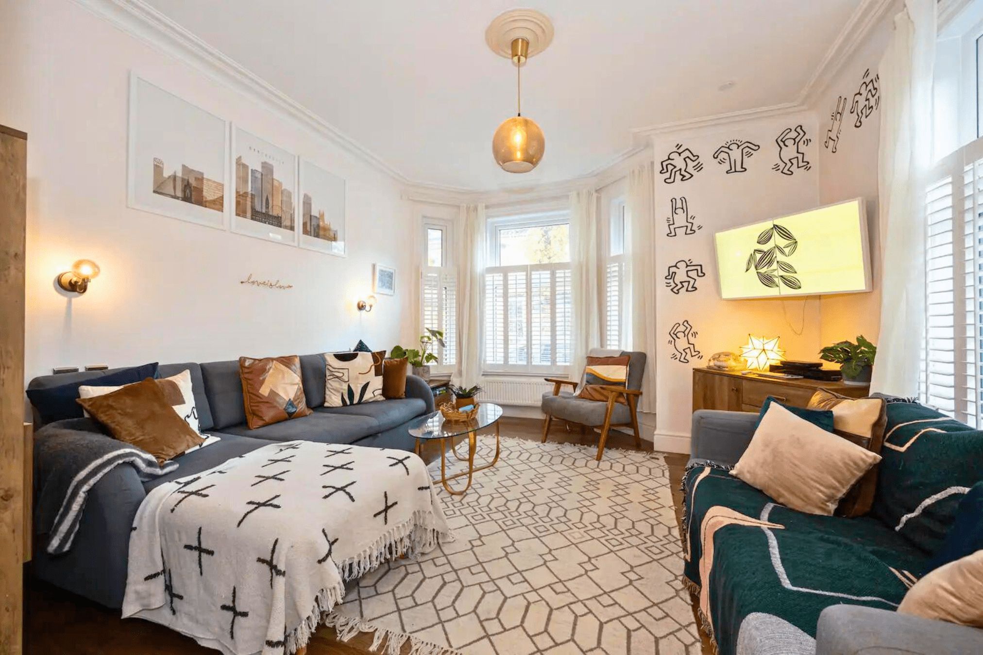 A living room with a sofa, armchair, and coffee table, a television, and wall art.
