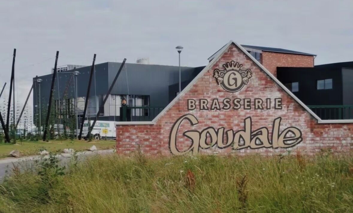 Skilt for 'Brasserie Goudale' med en moderne bygning i baggrunden.