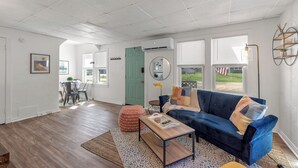 Ein geräumiges Wohnzimmer mit einem blauen Sofa, einem Couchtisch und einem Essbereich im Hintergrund.