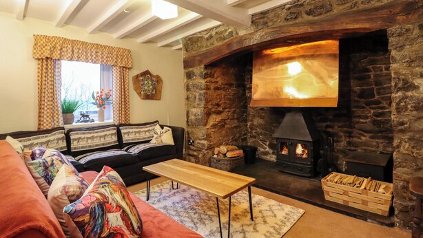 A cozy living room with a stone fireplace, a sofa, a coffee table, and a window with curtains. - Bryn Y Garreg Cottage - The Wireless Free Farm (Welshpool)