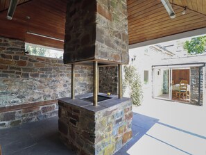 A stone-built outdoor kitchen area with a chimney, wooden ceiling, and a view of the adjacent building. - Bryn Y Garreg Cottage - The Wireless Free Farm (Welshpool)