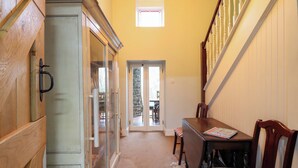 A narrow hallway with a wooden cabinet, a dining table with chairs, and a staircase with white balusters. - Bryn Y Garreg Cottage - The Wireless Free Farm (Welshpool)
